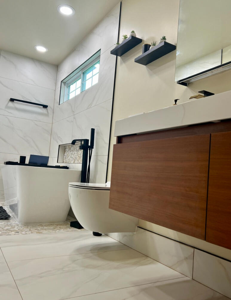 The redesigned space features a floating walnut vanity, large-format porcelain tile, integrated storage, matte black fixtures, and a sculptural freestanding tub—bringing warmth, simplicity, and everyday luxury together.